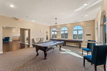 A room with a pool table and chairs.